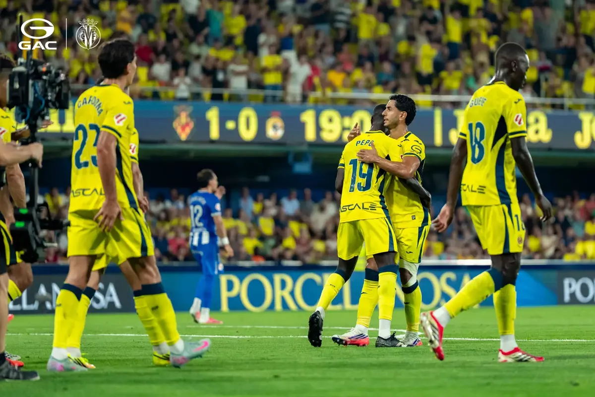Jucătorii Villarreal CF se îmbrățișează pe teren, cu tabela de marcaj în fundal